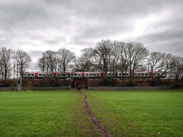 Passenger train crossing a small brick railway bridge over a muddy footpath on Chat Moss.