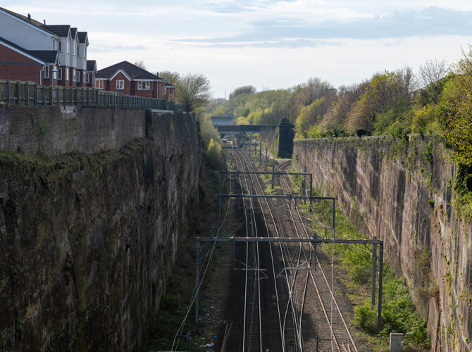 The electrified railway follows the floor of Olive Mount Cutting, framed by towering sandstone cliffs carved in the late 1820s.