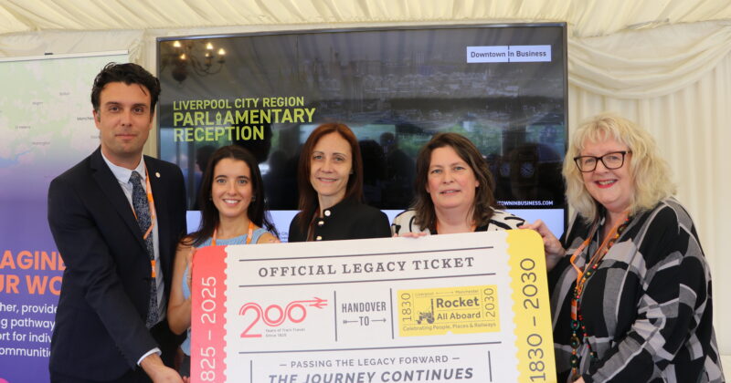 four people holding a large ticket with handover from Railway 200 to Rocket: All Board on it. They are standing infront of a large TV